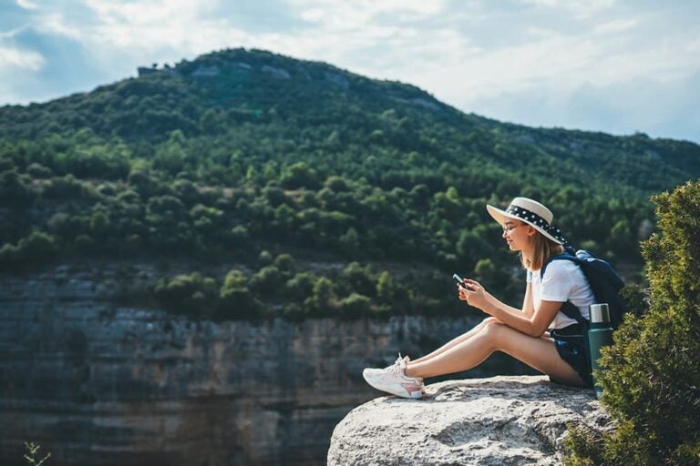旅行先の山頂でスマートフォンを操作する女性旅行者