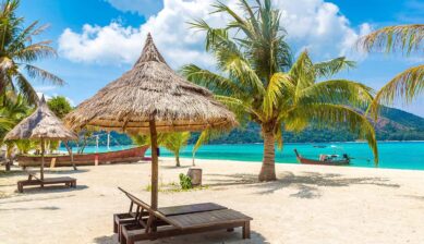 タイのビーチリゾートでヤシの木と草葺きのパラソル、エメラルドグリーンの海が広がる乾季の風景