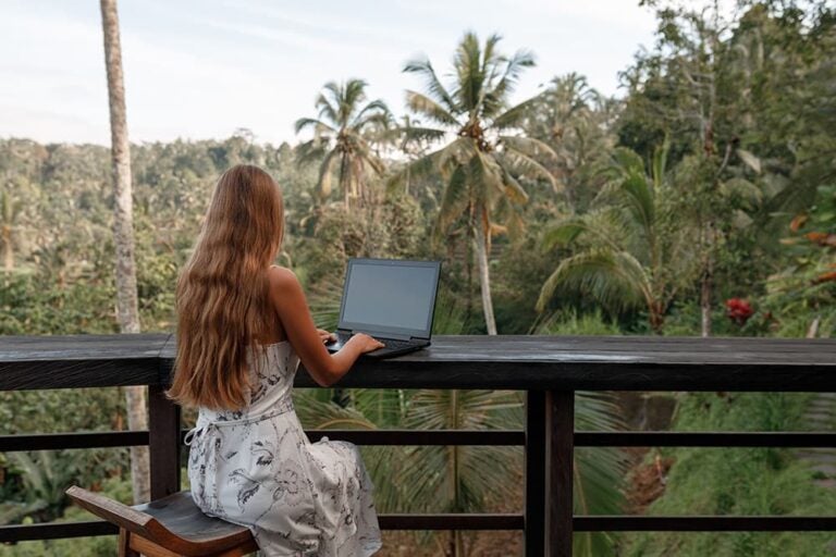 タイのリゾートテラスでノートパソコンを使う女性の後ろ姿。宿泊先で落ち着いて充電できる環境を示す一枚
