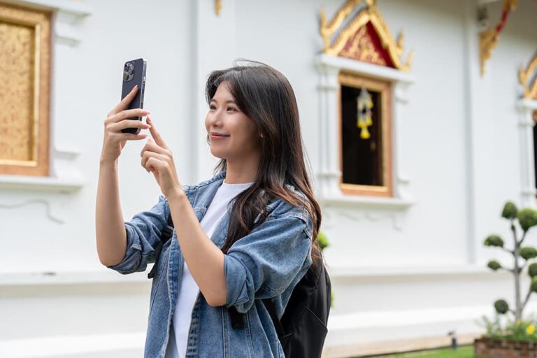 タイの寺院前でスマートフォンを手に写真を撮る女性旅行者の服装
