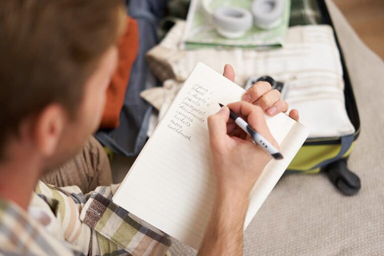 スーツケースの前で持ち物リストを書く旅行者。出発前の準備がニューヨーク旅行の安全につながる
