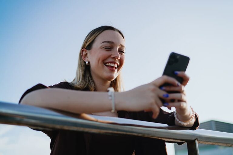 屋外でスマートフォンを見つめて笑う女性。電話番号なしでWhatsAppを使う際の利用シーンを示す一枚