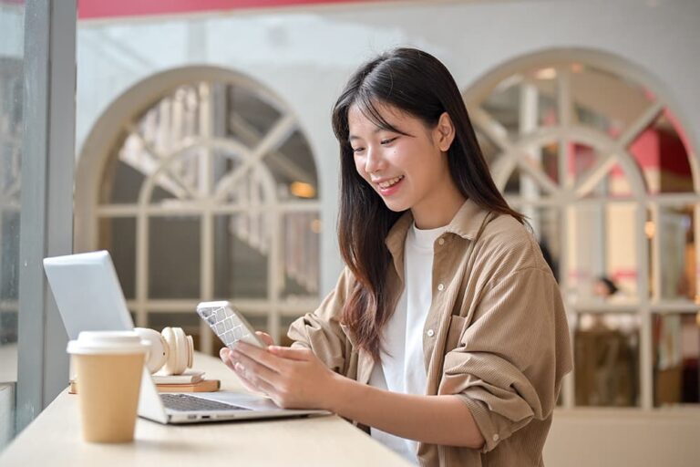 海外のカフェでスマートフォンを操作する笑顔の女性。eSIMを活用して旅行中もWhatsAppを使う場面を示す一枚