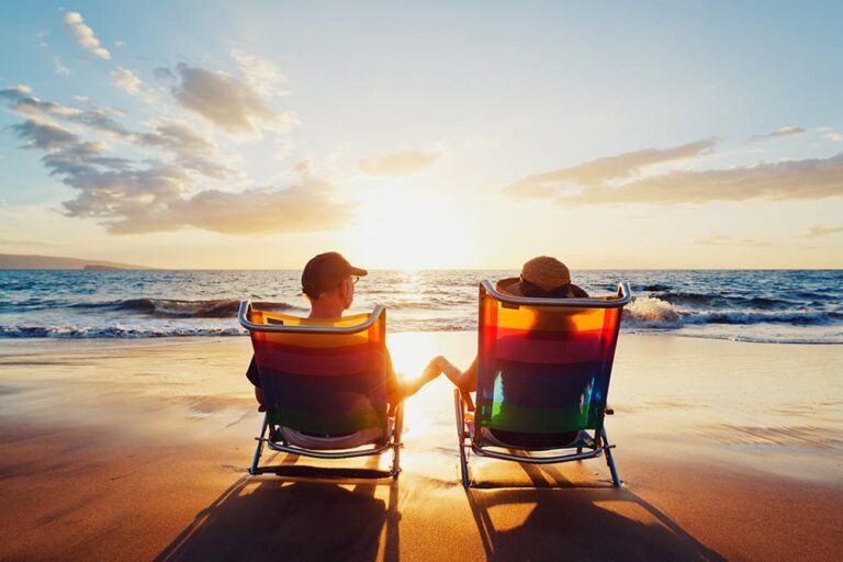ハワイのビーチで夕日を眺めながら手をつなぐカップル