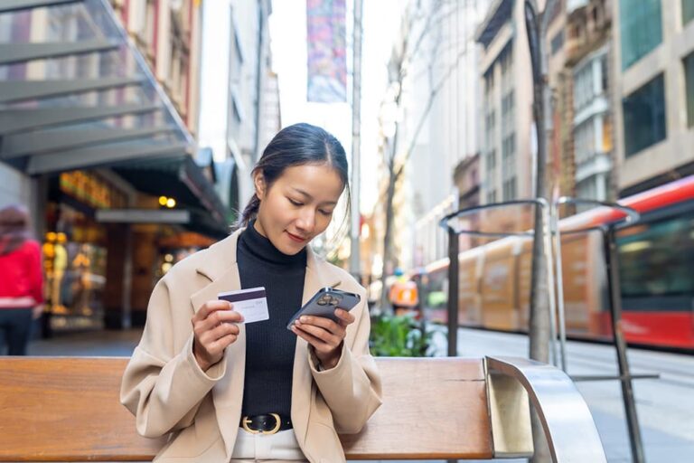 海外の街中でクレジットカードを手にスマートフォンのApple Payに登録する女性