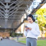 シドニーの橋の下でヘッドホンをつけ、スマホで音楽ストリーミングを利用する女性の画像