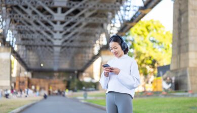 シドニーの橋の下でヘッドホンをつけ、スマホで音楽ストリーミングを利用する女性の画像