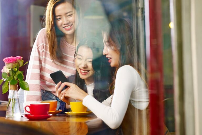 中国のカフェでスマートフォンを見ながら談笑する女性たち。外出先での充電やネット利用を楽しむ様子