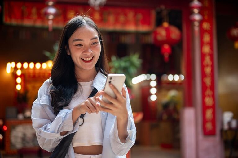 赤い提灯が飾られた中国の寺院でスマートフォンを使う女性旅行者。eSIMで快適にネット接続している様子