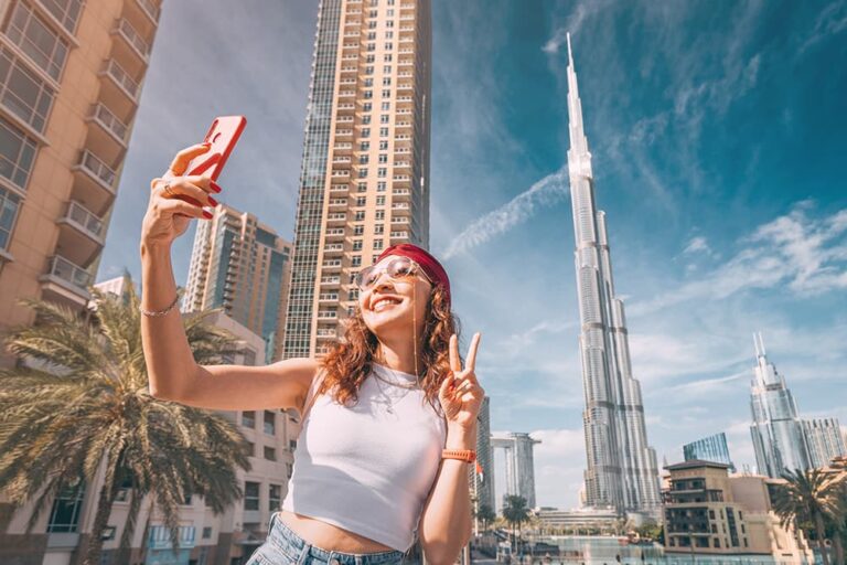 ブルジュ・ハリファを背景にスマホで自撮りを楽しむドバイ旅行中の女性