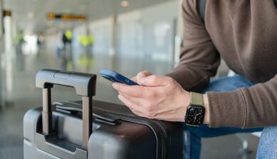空港でスーツケースの横に座り、スマートフォンで海外用通信手段を調べる旅行者