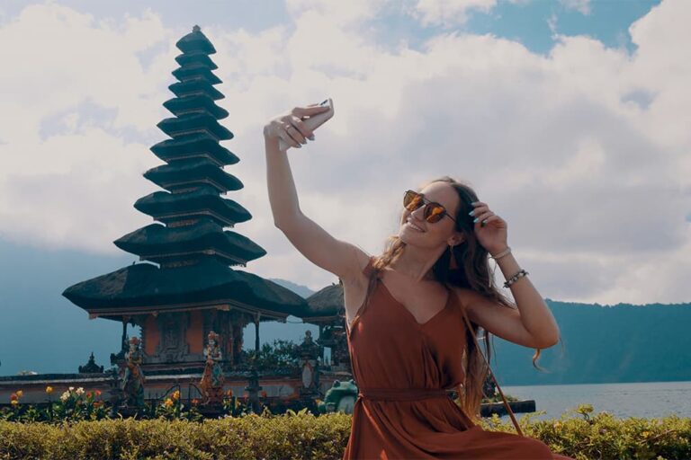 バリ島の湖畔の寺院を背景に、スマートフォンで自撮りを楽しむ女性旅行者