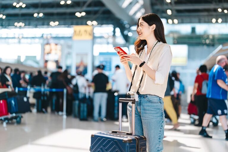 空港でスーツケースを持ち、スマートフォンを確認する旅行者