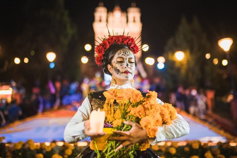 夜の死者の日にマリーゴールドの花束とろうそくを抱えるカトリーナメイクのメキシコ女性