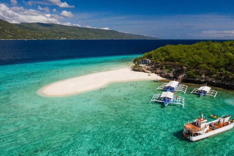 透き通った青い海に浮かぶセブ島スミロン島の白い砂浜とバンカーボートを上空から捉えた様子