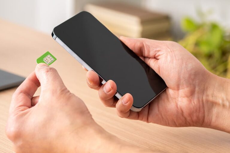 緑色の物理SIMカードを手に持ち、スマートフォンに挿入しようとする様子