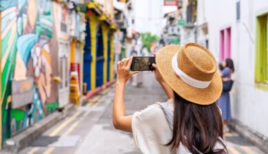 カラフルな壁画が並ぶシンガポールの街並みをスマートフォンで撮影する旅行者、子連れシンガポール旅行のイメージ