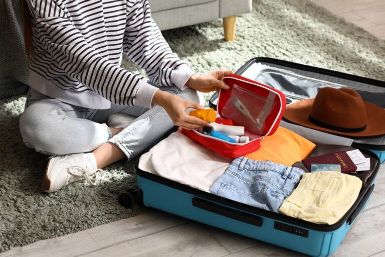 スーツケースに衣類やパスポートを詰め、常備薬の入った救急ポーチを準備する海外旅行前の薬の持ち込みの様子