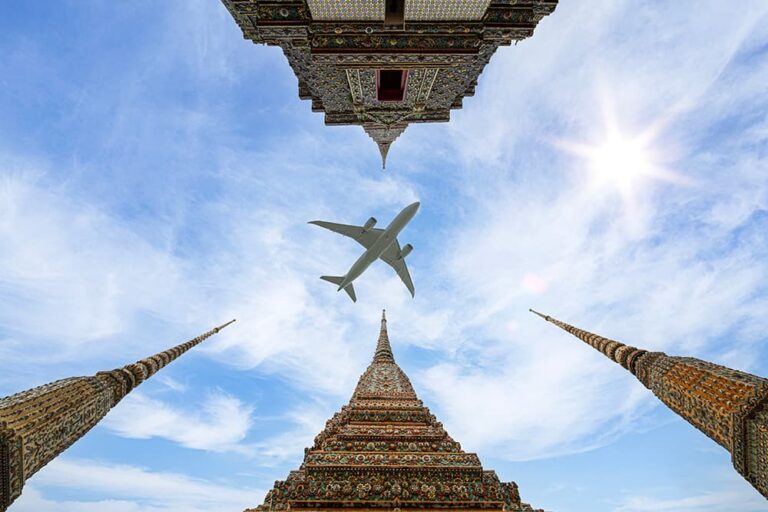 青空が広がるバンコクの寺院の仏塔上空を、タイ旅行のフライトを連想させる飛行機が飛び去る様子を真下から見上げた景色