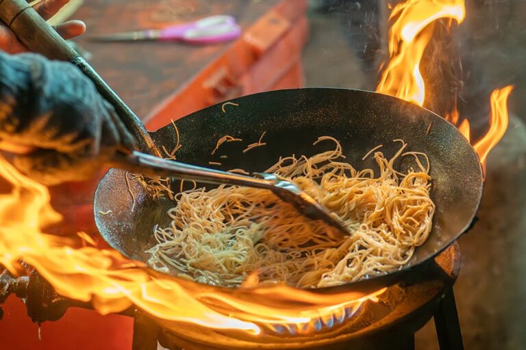 バンコクの屋台で激しい炎を上げて麺を炒める様子（旅行中の食費を安く抑えられるローカルフードのイメージ）