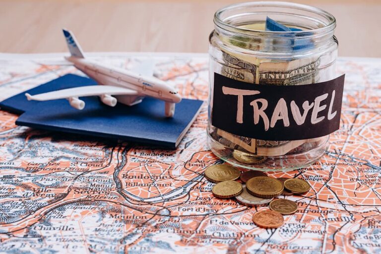 地図の上に置かれた飛行機の模型とTRAVELと書かれた貯金箱（バンコク旅行を安く抑えるための予算や節約のポイントを表現したイメージ）
