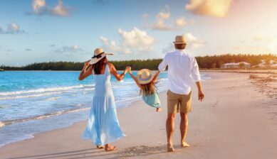 夕焼けに照らされた美しいビーチで、子どもと手をつないで波打ち際を歩く3人家族の後ろ姿。親子で最高の思い出を作る「子連れグアム旅行」を象徴する一枚