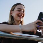 屋外でスマートフォンを手に持ち、YouTube動画を笑顔で楽しむ女性の様子