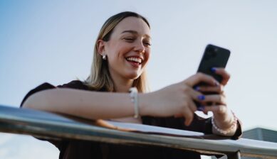 屋外でスマートフォンを手に持ち、YouTube動画を笑顔で楽しむ女性の様子