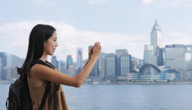 ビクトリア・ハーバーの高層ビル群を背景に写真を撮る香港旅行者