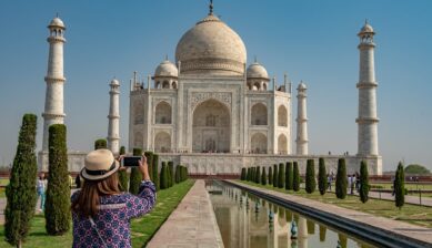 タージ・マハルを背景にスマートフォンで写真を撮るインド旅行者