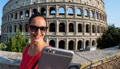 ローマのコロッセオを背景にスマホを使うイタリア旅行者の女性