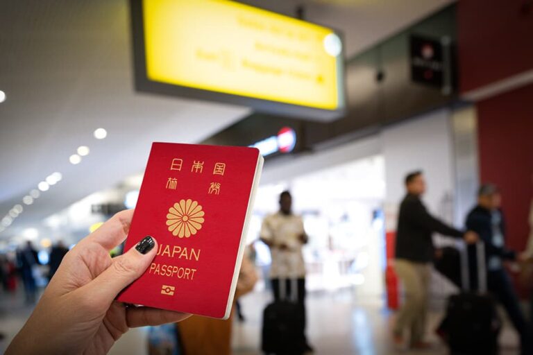 シンガポール・チャンギ空港の到着ロビーで日本のパスポートを手に持つ旅行者。背景には案内表示と行き交う人々が写っている