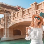 海外旅行先で石造りの橋を背景にスマートフォンを掲げる女性の旅行イメージ