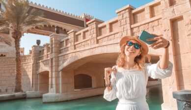 海外旅行先で石造りの橋を背景にスマートフォンを掲げる女性の旅行イメージ