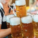 民族衣装姿の女性が両手で複数の大きなビールジョッキを一度に運んでいる様子