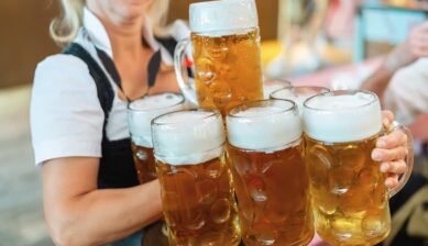 民族衣装姿の女性が両手で複数の大きなビールジョッキを一度に運んでいる様子