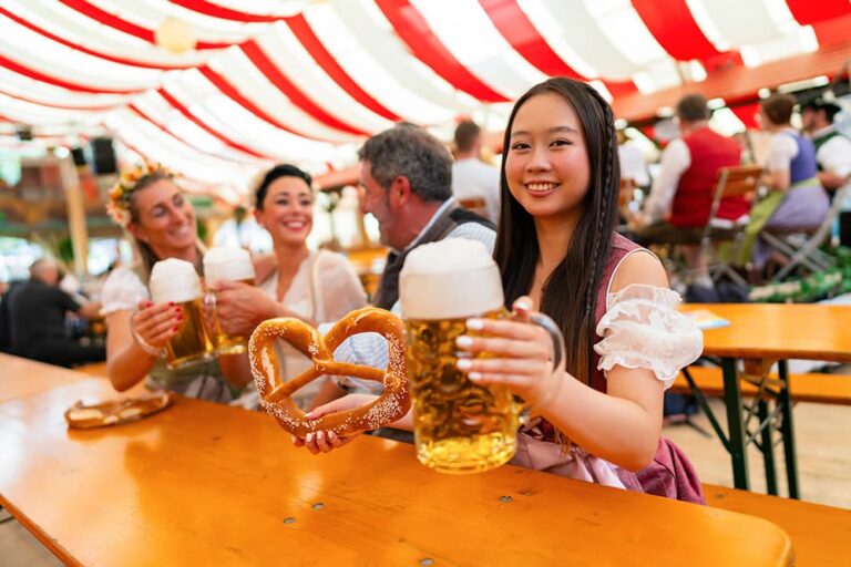 民族衣装を着た女性がオクトーバーフェストのビアテントでプレッツェルとビールを手に微笑む様子