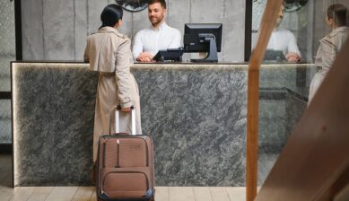 香港空港のラウンジ受付でスタッフの案内を受けるスーツケースを持った旅行者