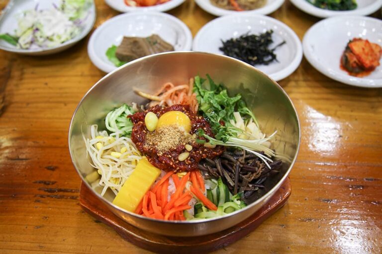真鍮の器にご飯、色とりどりの野菜、ナムル、卵黄、コチュジャンを盛り付けたビビンバ