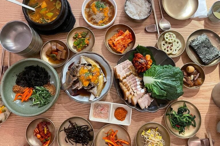 ゆで豚を葉野菜やキムチと一緒に味わうポッサムと韓国の小皿料理が並ぶ食卓