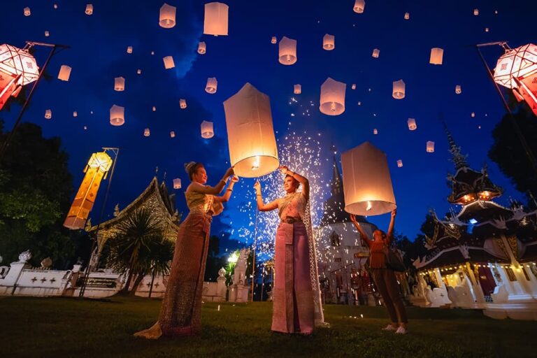 タイ・チェンマイの寺院で夜空にコムローイ（灯篭）を打ち上げる女性たちとイーペン祭りの光景