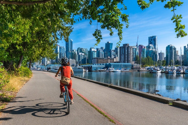 バンクーバーの街並みと港を眺めながらスタンレーパーク沿いを自転車で走る観光客