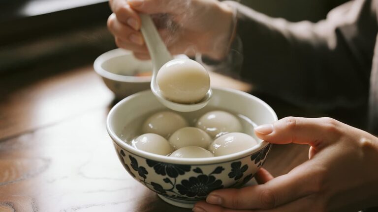 温かいスープが入った花柄のお椀から、上海スイーツの湯圓（餡入り団子）をレンゲですくい上げている様子。ほんのりと湯気が立ち上り、もちもちとした質感が伝わる