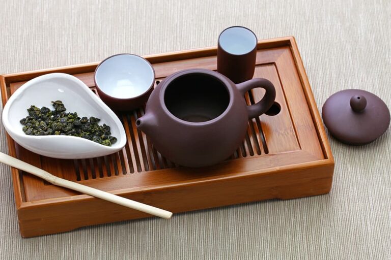 木製の茶盤の上に用意された、中国を代表する緑茶「龍井茶（ロンジンチャ）」の茶葉と本格的な中国茶器セット。白い器に盛られた茶葉や茶壺（急須）が並んでいる様子