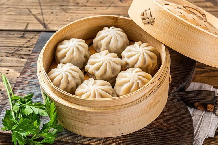 木のテーブル上のせいろに並べられた、上海名物の焼き小籠包（生煎包）。傍らには緑の香草が添えられている様子