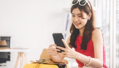 海外旅行用のスーツケースのそばでスマートフォンを操作する女性