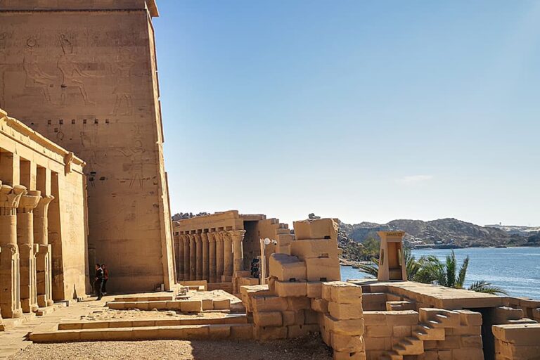 エジプトの歴史的な観光地であるアスワンのフィラエ神殿にて、壁面にレリーフが残る古代遺跡と、その奥に広がるナイル川の穏やかな風景