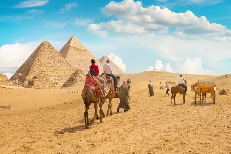エジプトの代表都市ギザの砂漠で、ピラミッドを背景にラクダに乗って観光を楽しむ旅行者の様子
