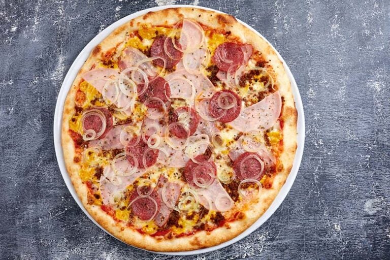 ヨーロッパ旅行で手軽な食べ物として人気の、イギリス・ロンドンにある格安ピザ店「ICCO」のピザ。サラミやハム、スライスされた玉ねぎがたっぷりとトッピングされた焼きたての丸いピザが、白いお皿にのっている様子