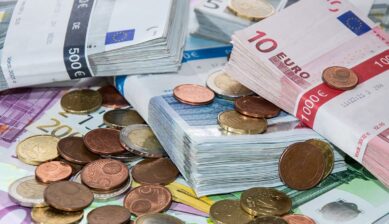 積み重ねられたユーロ紙幣の束と、周囲に広がるユーロ硬貨